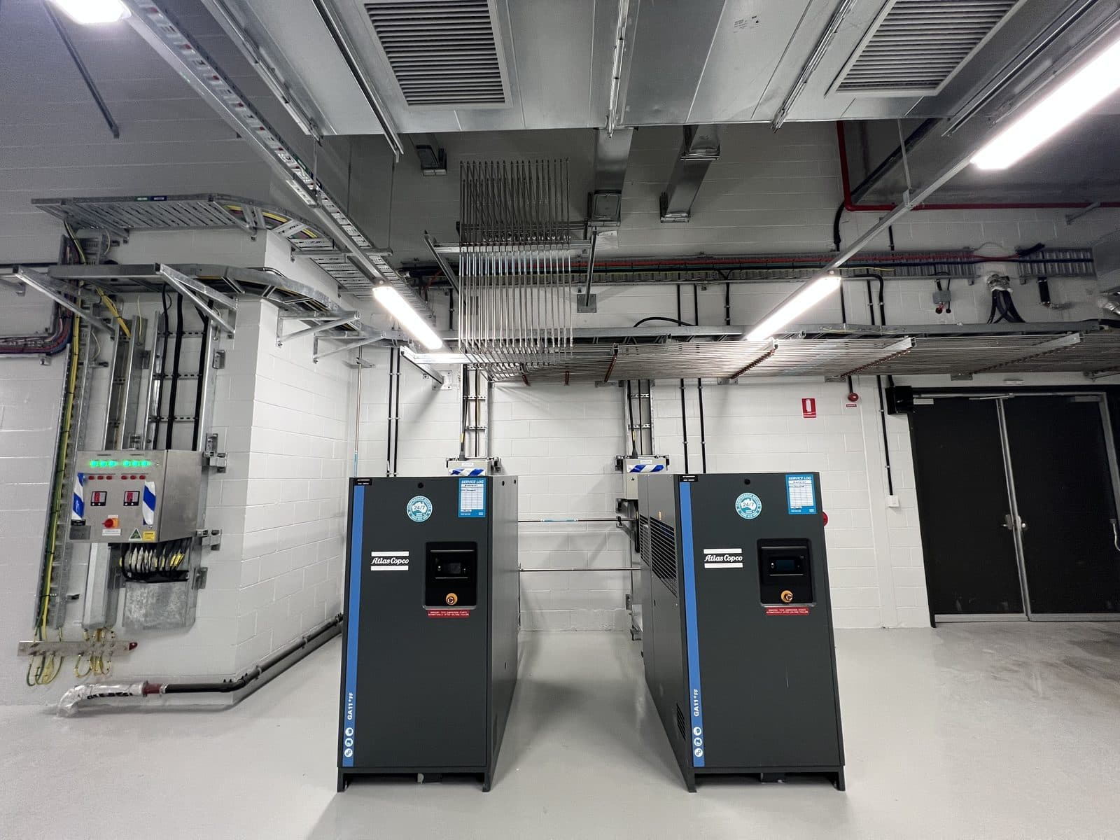 Wall-mounted control panel and Atlas Copco compressors in the Sydney Metro compressed air plant room